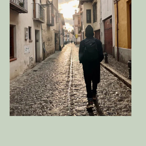 A lone figure walking down a sunlit cobblestone street
